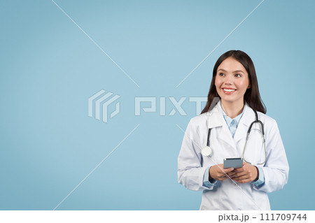 Happy woman doctor in white uniform with phone looking at free space 111709744