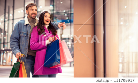 Happy young couple pointing standing with shopping bags outside mall 111709917