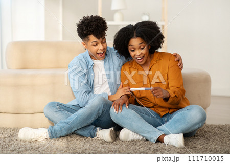 An overjoyed young couple sits on the floor with a positive pregnancy test An overjoyed young couple sits on the floor with a positive pregnancy test 111710015