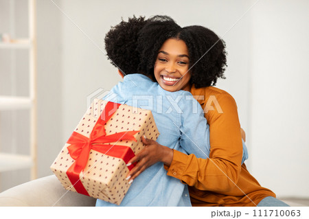 A woman with a beaming smile gives a warm hug to a person while holding a heart-patterned gift box A woman with a beaming smile gives a warm hug to a person while holding a heart-patterned gift box 111710063