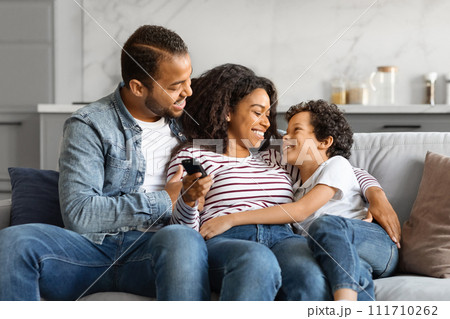 Relaxed black family lounging on the couch with remote in hand Relaxed black family lounging on the couch with remote in hand 111710262