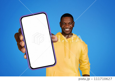 Smiling black man holds cellphone empty screen on blue background Smiling black man holds cellphone empty screen on blue background 111710627