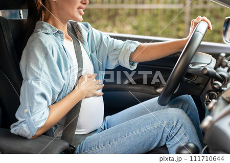 Cropped of pregnant lady driver navigating car vehicle touching belly Cropped of pregnant lady driver navigating car vehicle touching belly 111710644
