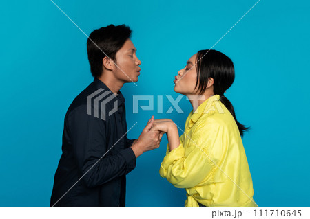 Happy young japanese guy and woman in casual kisses, isolated on blue studio background Happy young japanese guy and woman in casual kisses, isolated on blue studio background 111710645
