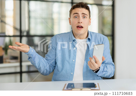 Shocked confused sad millennial european guy manager hold on hand free space and phone 111710683