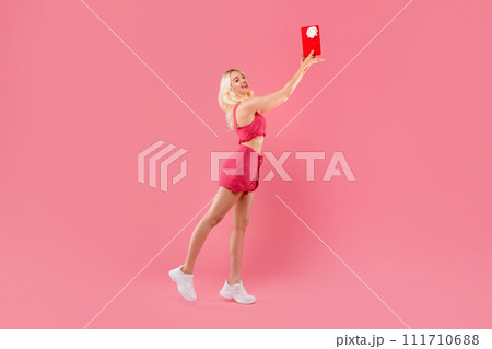 Ecstatic young woman tossing gift in the air, pink background 111710688