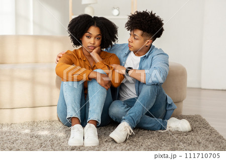 A young woman appears troubled and contemplative while sitting on the floor A young woman appears troubled and contemplative while sitting on the floor 111710705