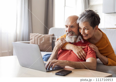 Smiling Senior Spouses Spending Time With Laptop In Living Room 111710953