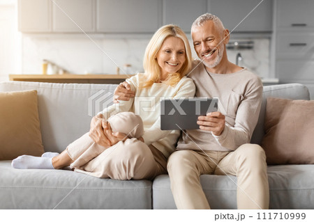 Positive beautiful loving senior spouses using digital tablet at home 111710999