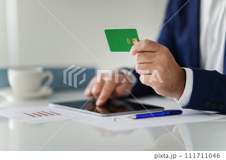 A businessman in a navy suit is making an online payment using a green credit card and a digital tablet A businessman in a navy suit is making an online payment using a green credit card and a digital tablet 111711046