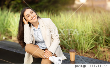 Relaxed glad young professional caucasian woman sits on bench with cup of coffee Relaxed glad young professional caucasian woman sits on bench with cup of coffee 111711072