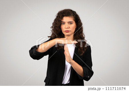 Serious businesswoman in suit making timeout gesture, symbolizing the need for break or pause 111711074