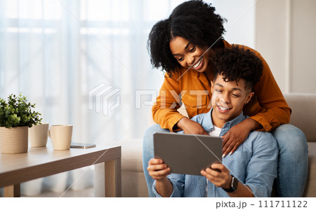 Happy young african american man and lady, hugs, use tablet, watch video on device Happy young african american man and lady, hugs, use tablet, watch video on device 111711122