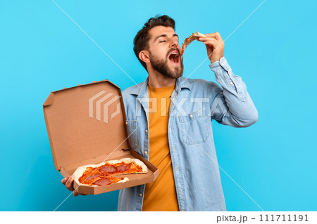 Caucasian man biting pizza slice while holding delivery box, studio Caucasian man biting pizza slice while holding delivery box, studio 111711191