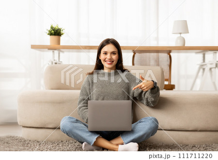 Happy young european woman pointing at laptop, home interior Happy young european woman pointing at laptop, home interior 111711220