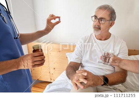 Nurse give pill to serious senior caucasian man in bedroom interior Nurse give pill to serious senior caucasian man in bedroom interior 111711255