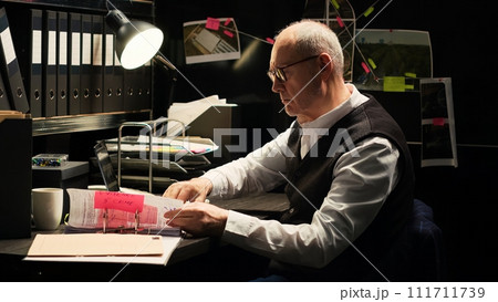 Law officer examine police documents to uncover crucial case evidence, detective work in incident room. Experienced inspector undertaking investigatory services, forensic science. Handheld shot. 111711739