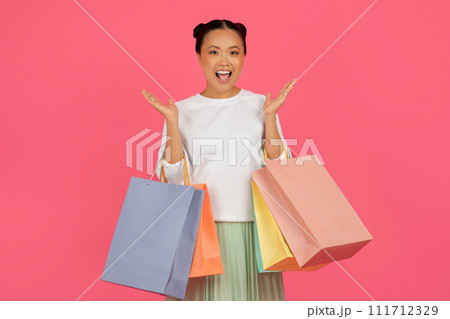 Joyful asian woman holding shopping bags and raising her hands with excitement Joyful asian woman holding shopping bags and raising her hands with excitement 111712329