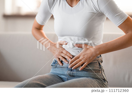 Unrecognizable young woman touching aching stomach feeling abdominal pain indoor 111712360