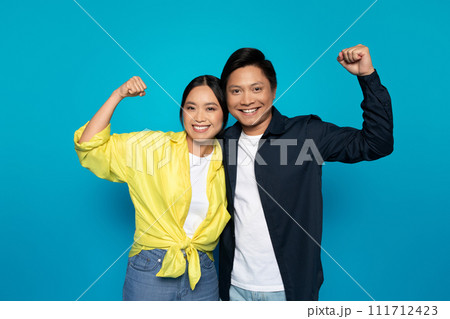 Glad millennial japanese couple in casual rise fists, celebrate victory, success 111712423