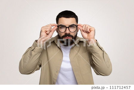 Serious smart millennial middle eastern man adjusting glasses, focused gaze, with thoughtful expression 111712457