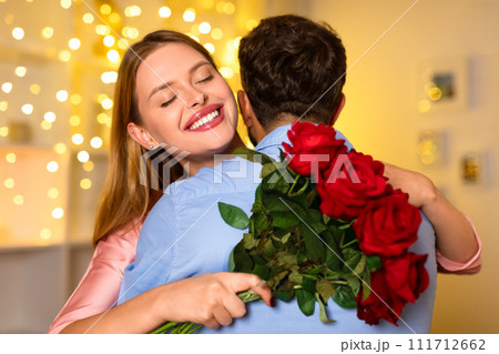 Joyful woman embracing man, holding red roses with festive lights 111712662