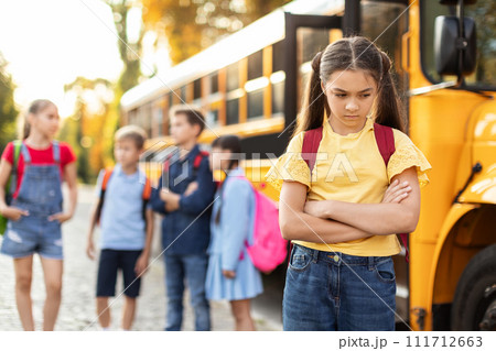 Unhappy young girl standing by herself next to yellow school bus Unhappy young girl standing by herself next to yellow school bus 111712663