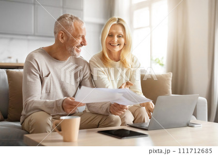 Smiling retired couple holding papers, calculating domestic bills 111712685