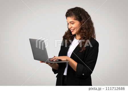 Engaged young businesswoman focused on typing on laptop, demonstrating efficient workflow and connectivity 111712686