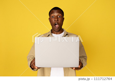 Happy excited millennial black guy in casual with laptop and open mouth, rejoices success 111712764