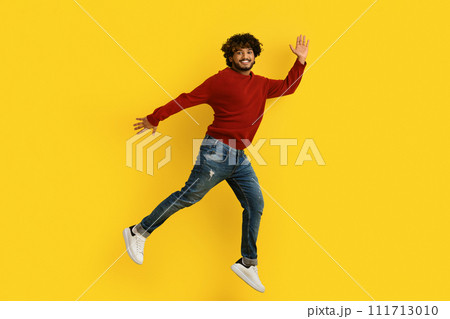 Excited young indian guy jumping over yellow background Excited young indian guy jumping over yellow background 111713010
