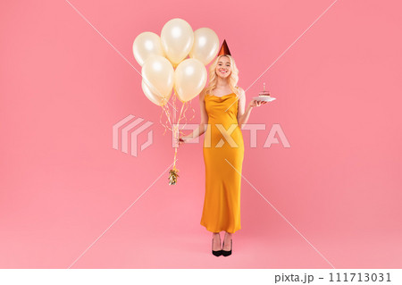 Elegant young woman with balloons and cake on pink background 111713031