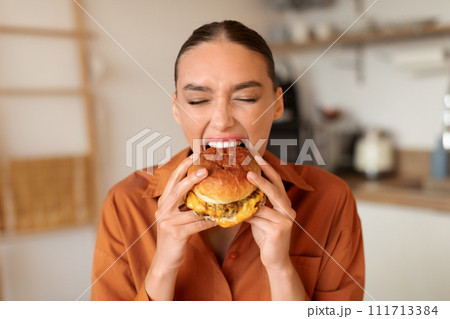 Woman eagerly biting into a savory burger at home 111713384