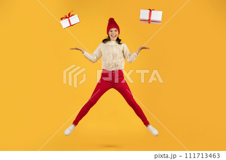 woman in knitted cap jumps with two presents, yellow background woman in knitted cap jumps with two presents, yellow background 111713463