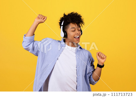Happy black guy dancing with headphones on yellow background Happy black guy dancing with headphones on yellow background 111713723
