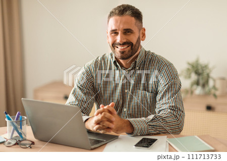 middle aged man smiling as working on laptop in office 111713733