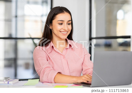 Cheerful millennial arab woman manager typing on laptop planning day Cheerful millennial arab woman manager typing on laptop planning day 111713863