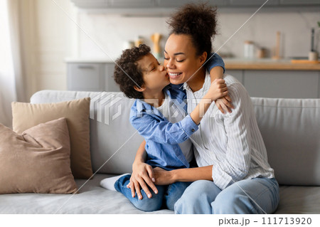 Preteen boy gives loving kiss on the cheek to his joyful mother 111713920