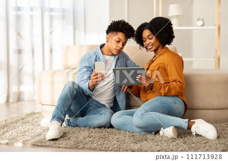 Casually dressed in denim, a young couple sits on a plush rug, engrossed in their devices 111713928