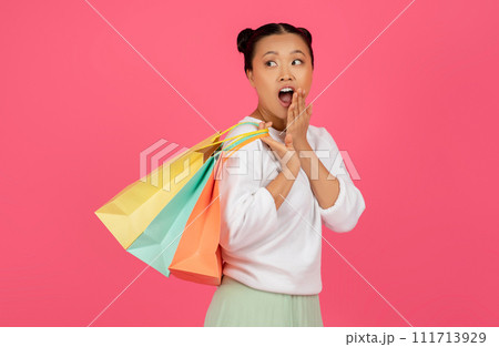 Excited asian female with shopping bags touching her face in surprise Excited asian female with shopping bags touching her face in surprise 111713929