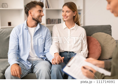 Cheerful millennial couple seated on therapist's couch sharing smiles Cheerful millennial couple seated on therapist's couch sharing smiles 111714091