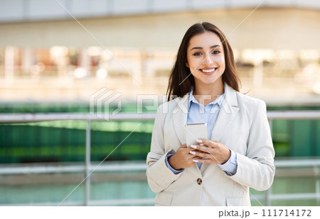 Glad pretty confident young caucasian woman in suit enjoy work, typing on smartphone outdoors 111714172