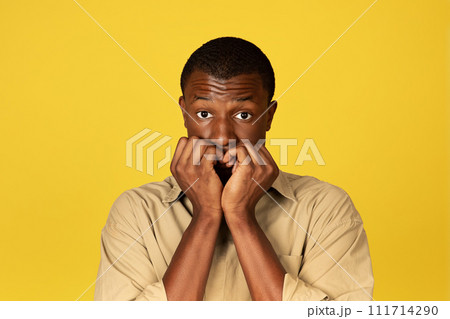 Shocked confused shy young black man in casual bites fingers Shocked confused shy young black man in casual bites fingers 111714290