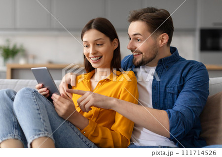 Excited caucasian spouses using digital tablet on the couch 111714526