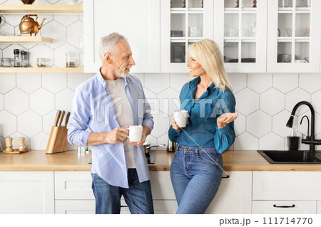 Smiling senior man and woman drinking coffee together in modern kitchen interior Smiling senior man and woman drinking coffee together in modern kitchen interior 111714770
