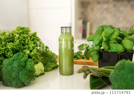 Bottle of nutritious green smoothie standing on table amidst herbs Bottle of nutritious green smoothie standing on table amidst herbs 111714791