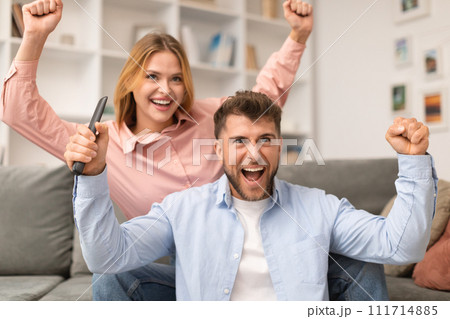 Excited Couple Watching TV And Shaking Fists In Joy Indoors 111714885