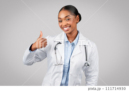 Cheerful pretty millennial black lady doctor in white coat make thumb up sign with hand 111714930