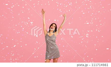 Vibrant young woman in a glittery dress with a wide smile, arms joyfully raised Vibrant young woman in a glittery dress with a wide smile, arms joyfully raised 111714981
