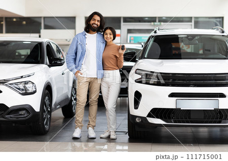 Smiling millennial indian couple standing next to new car Smiling millennial indian couple standing next to new car 111715001